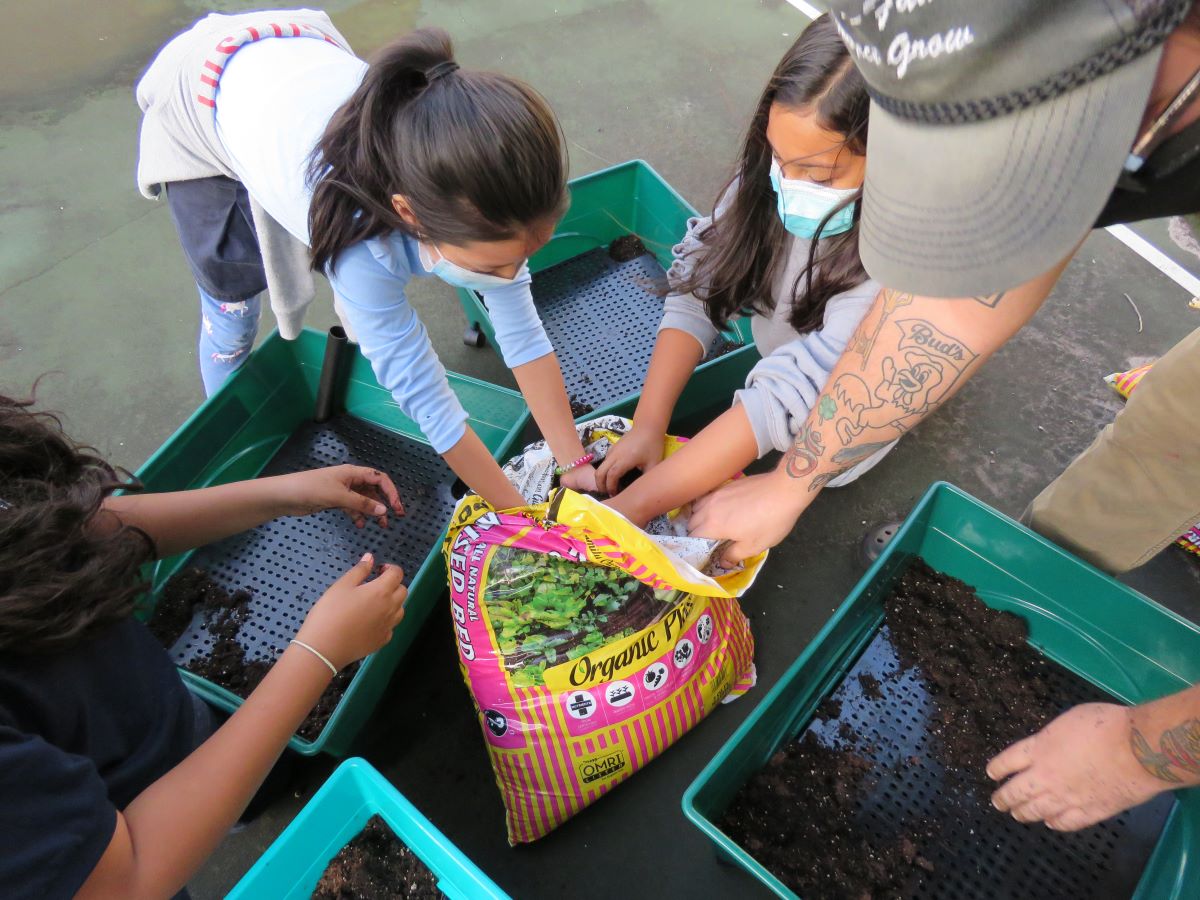 Group of people reaching hands into a bag of soil